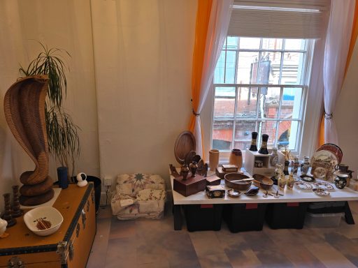 Display of various wooden sculptures and artifacts near a window with orange curtains.