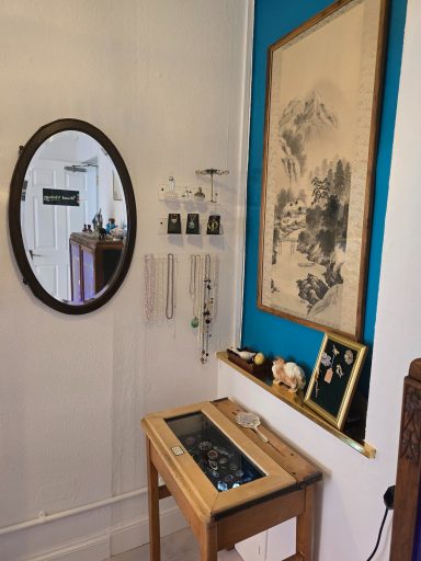 Wall display featuring a mirror, framed artwork, photographs, and decorative items on a table.