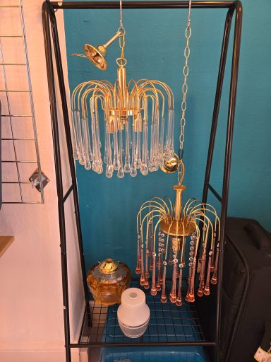 Two decorative chandeliers with gold accents hanging on a display rack against a blue wall.
